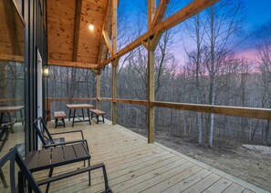 A wooden deck with tables and chairs, overlooking a forested area. - Timberline Retreat | Hocking Hills, Hot Tub (Creola)
