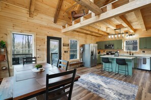 A wooden cabin interior with a dining area, kitchen, and bar seating.