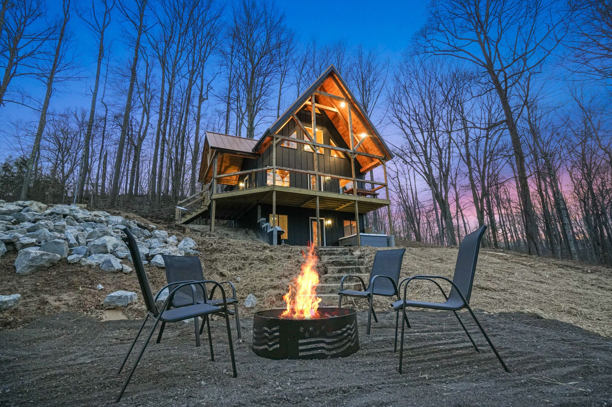 A cabin with a fire pit and chairs in front, surrounded by trees.