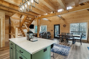 A wooden cabin interior with a kitchen area, dining table, and a staircase. - Timberline Retreat | Hocking Hills, Hot Tub (Creola)
