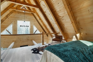 A high-ceilinged wooden room with a bed, a chair, and a hanging light fixture.