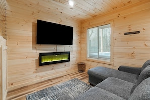 A cozy cabin interior with a flat-screen TV mounted on the wall, a fireplace below it, and a sign indicating a 'Campfire' area.