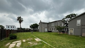 A residential backyard with a lawn, a palm tree, and a two-story house. - Spacious 6-bedroom house in lovely Corpus Christi 1 block from Ocean Dr. (Corpus Christi)