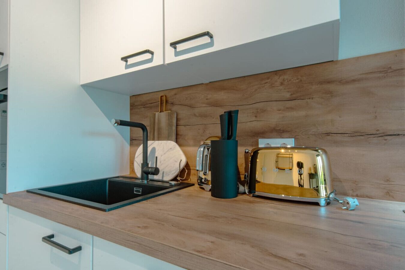 Eine moderne Küche mit Holzarbeitsplatte, einem schwarzen Spülbecken, einer Marmor-Spritzschutzwand und einem Toaster im Vintage-Design.