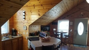 Un chalet confortable doté d’un coin cuisine avec des murs en bois, une table à manger avec des chaises et un téléviseur fixé au mur.