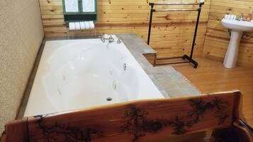 A wooden-paneled bathroom with a large bathtub, a wooden bench, a towel rack, and a sink.