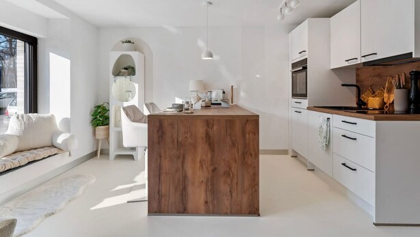 Una cocina moderna con armarios blancos, una isla de madera y una zona de comedor con sofá y sillas blancos.