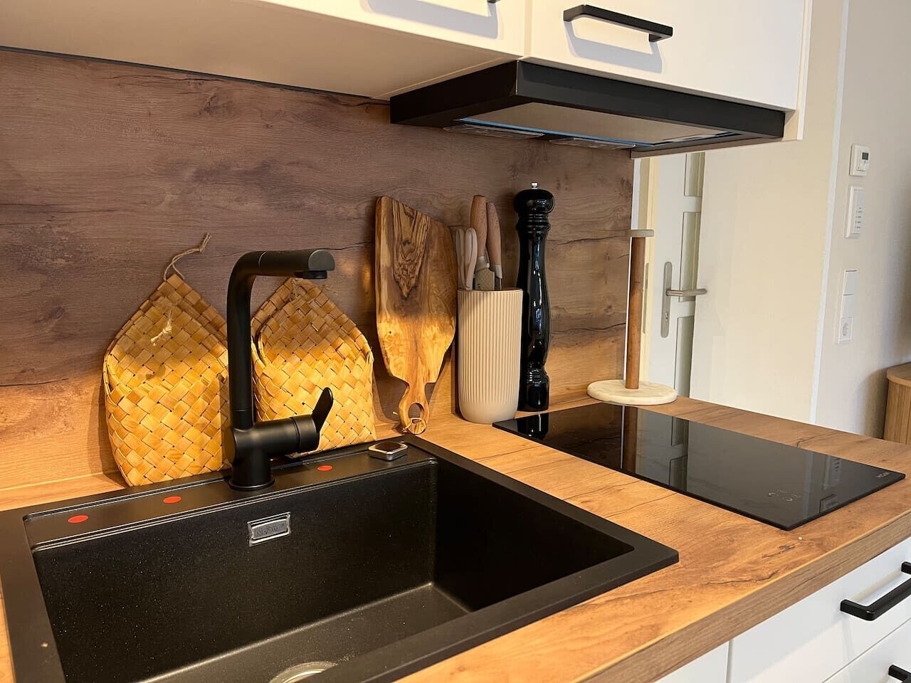 Una cucina moderna con lavello nero, piano di lavoro in legno e piano cottura integrato.