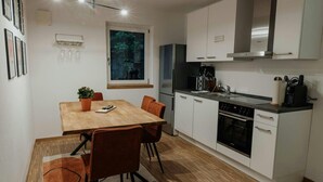 A compact kitchen with white cabinets, a wooden dining table, and a window with a view of trees. - Passau Appartements|Central|Stylish|Comfortable (Passau)