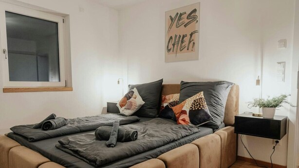 A modern bedroom with a bed, pillows, a nightstand, a lamp, and a wall art piece. - Passau Appartements|Central|Stylish|Comfortable (Passau)