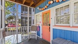 A covered porch with a glass table and chairs, a red door, and a view of the street. - Clove Coastal Cottage - Steinhatchee Landing (Steinhatchee)