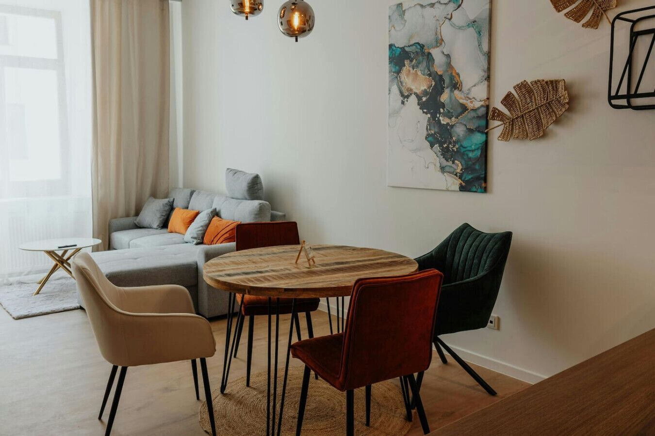 Een moderne woonkamer met een grijze bank, een ronde houten tafel en rode en zwarte stoelen.