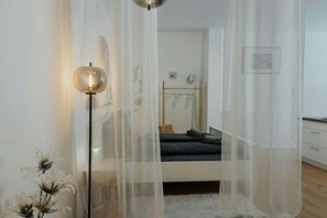 A bedroom with a bed, a bedside table, a hanging light fixture, and sheer curtains.