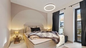 A modern bedroom with a bed, a bedside lamp, a window with curtains, and a view of the outdoors.