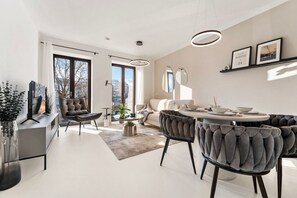 Una sala de estar moderna con un sofá, sillas, una mesa de comedor y un televisor.