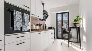 A modern kitchen with white cabinets, black appliances, and a window overlooking a cityscape.