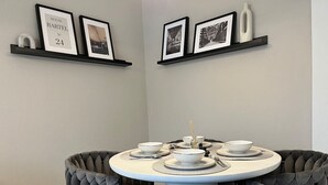 A dining area with a round table set for four, surrounded by upholstered chairs. There are framed pictures on the walls above the table.