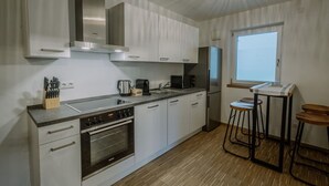 Una cocina moderna con armarios blancos, electrodomésticos de acero inoxidable, horno integrado y una ventana que proporciona luz natural.