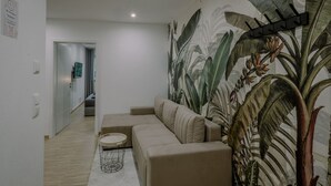 Un salón moderno con un sofá color beige, una mesa de centro redonda y un amplio mural con temática tropical en la pared.