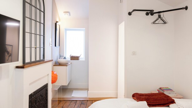 A bedroom with a bed, a window, a bedside table with books, and a hanging light fixture. - Studio Secundo (Metz)