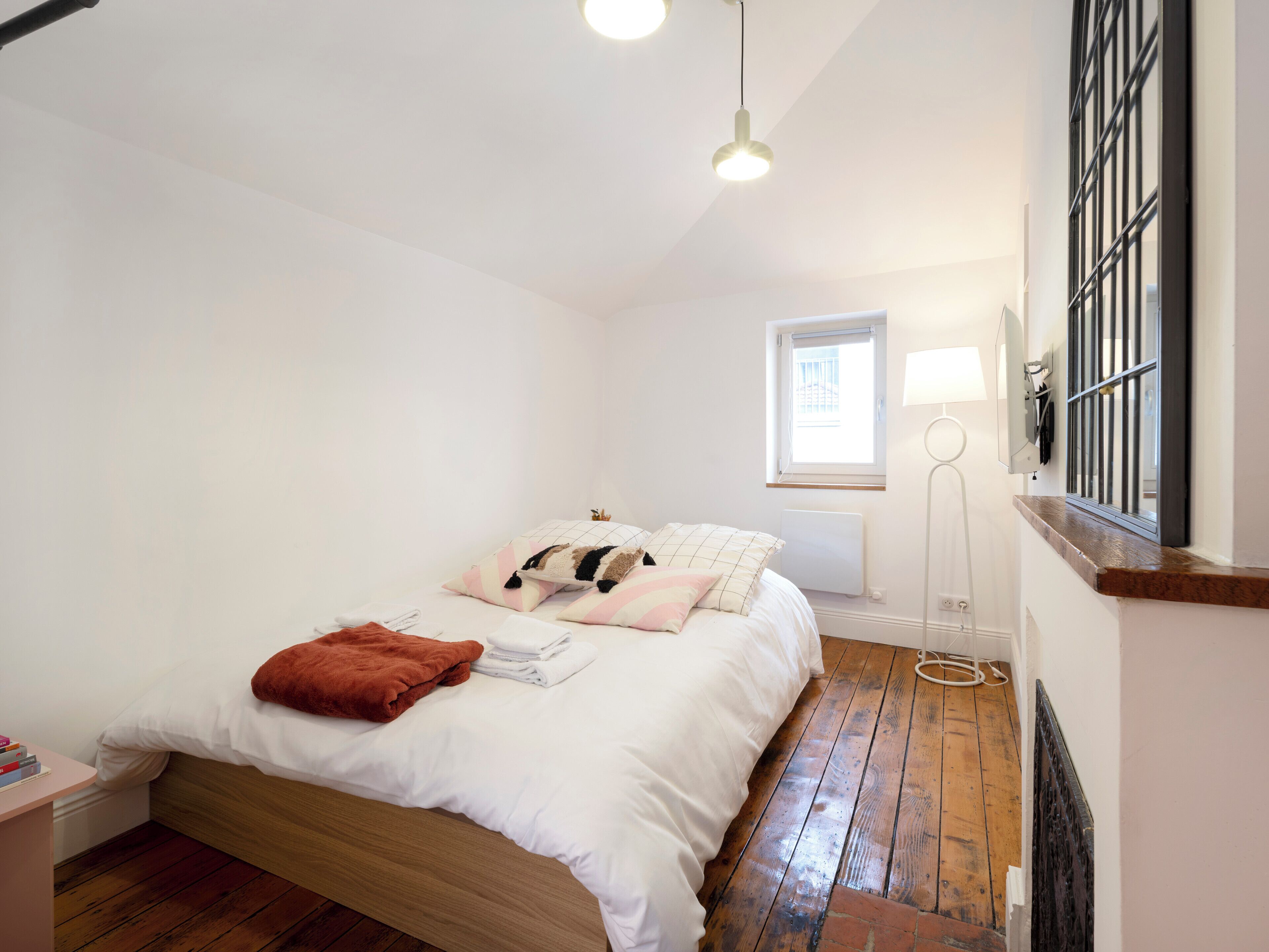 Ein Schlafzimmer mit einem hölzernen Bett, weißer Bettwäsche, einer roten Tagesdecke und einem Fenster mit Blick.