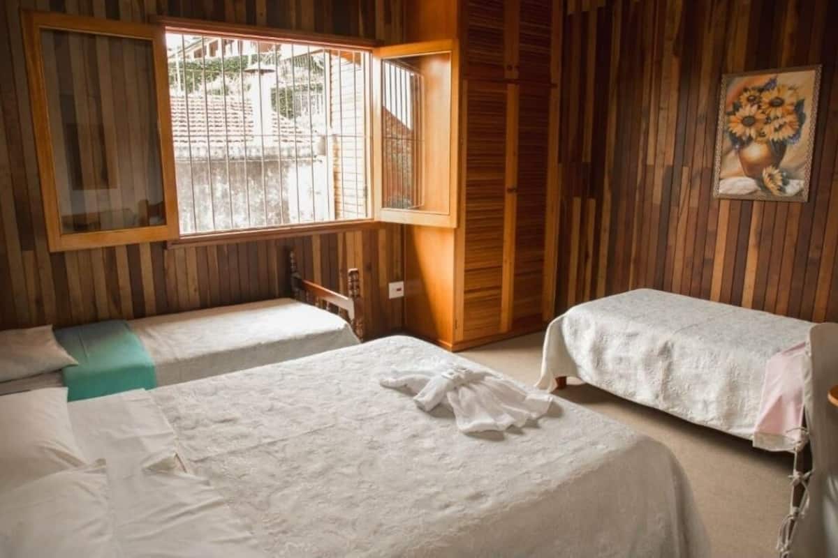 A room with two beds, wooden walls, a window with bars, and a painting of sunflowers.