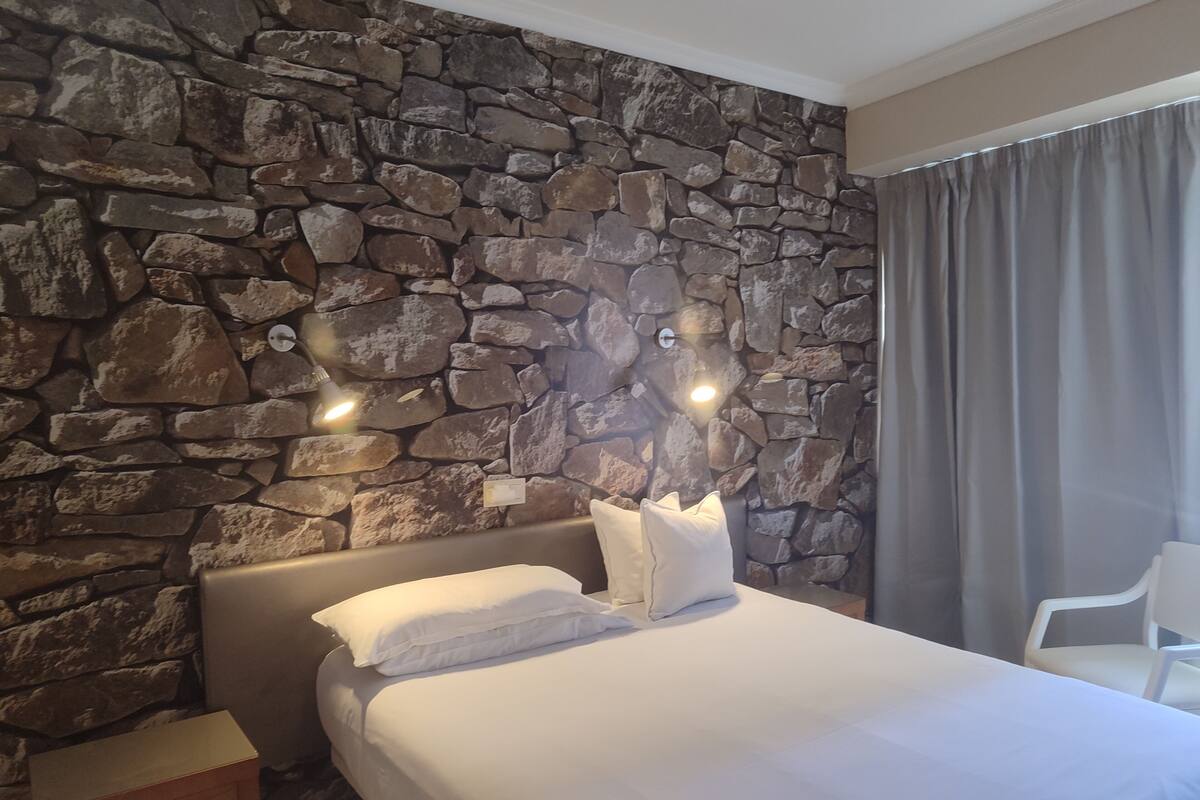 Une chambre d’hôtel avec un mur en pierre, un lit avec du linge de lit blanc, une table de chevet et une chaise.
