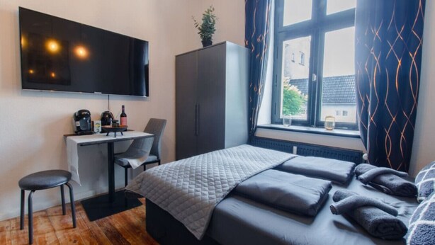 A hotel room with a bed, a desk with a chair, a television, and a window with curtains. - Travelbase/Monteurswohnung Anklam (Anklam)