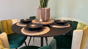Een eettafel gedekt met zwarte borden, een roze vaas met een plant en een paar kaarsen.