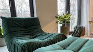Een moderne slaapkamer met een met groen bekleden bed, een potplant en uitzicht door grote ramen.