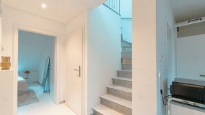A modern interior with a staircase leading to a second floor, a door with a handle, and a small table with a lamp. - Stuttgart Lux Living |Stylish Living in the Center (Stuttgart)