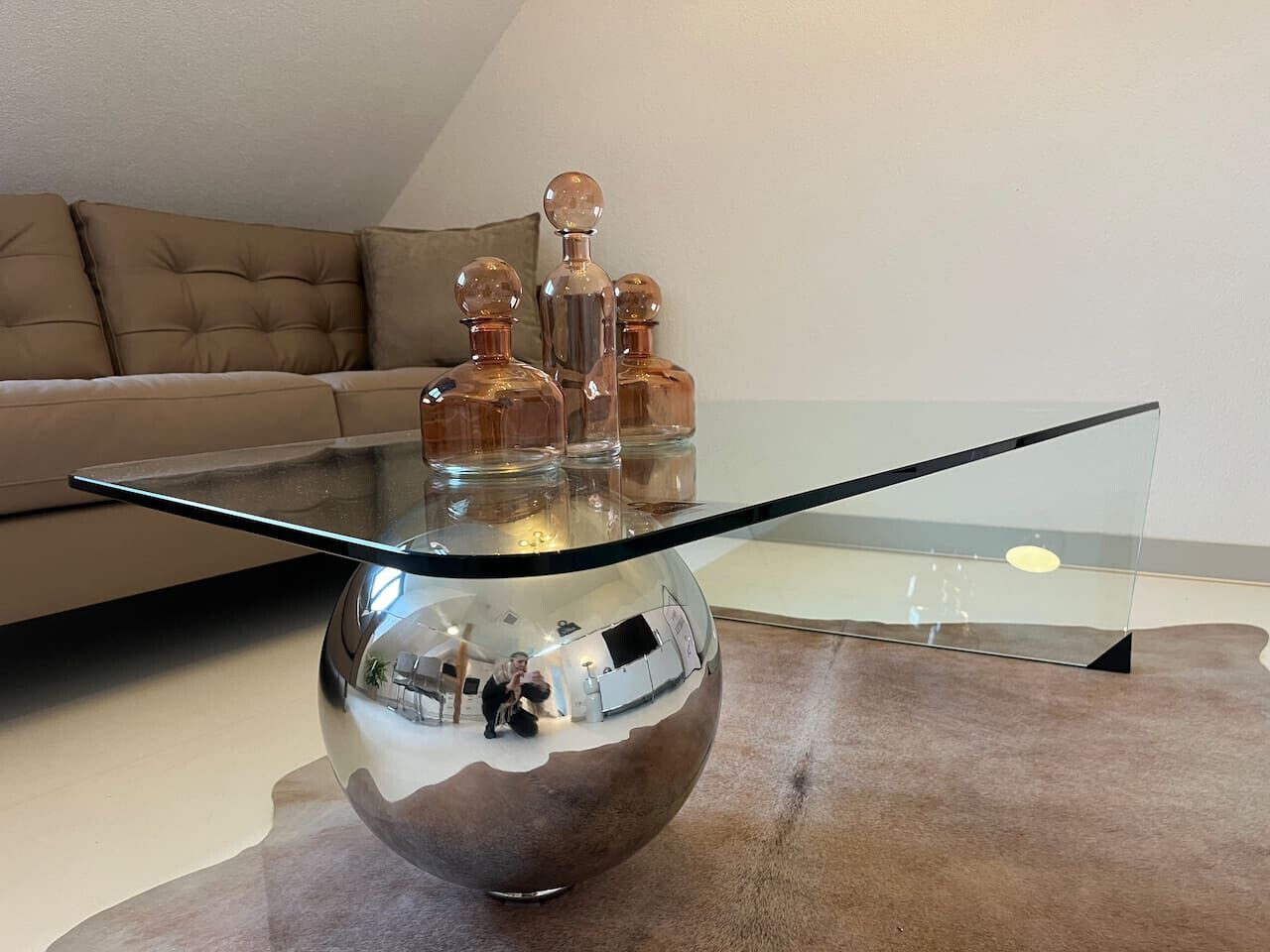 Ein modernes Wohnzimmer mit einem Glastisch, einer Couch und dekorativen Flaschen.