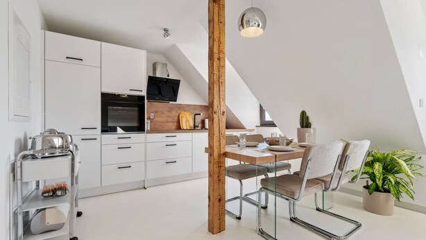 A modern kitchen with white cabinets, a wooden accent wall, a dining area with a table and chairs, and a ceiling light fixture. - Stuttgart Lux Living |Stylish Living in the Center (Stuttgart)