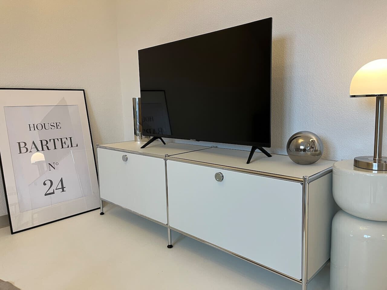 Ein modernes Zimmer mit einem weißen Schrank, einem Flachbildfernseher, einem gerahmten Schild und einer Lampe.