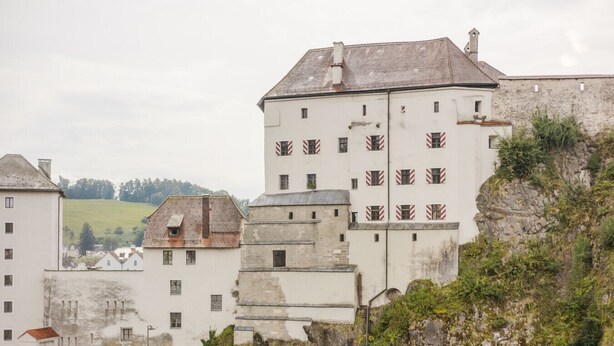 Ein mehrstöckiges Gebäude mit weißer Fassade und roten Fensterläden, umgeben von Grünflächen und anderen Gebäuden.