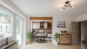 Eine moderne Küche mit Holzausstattung, ein Essbereich mit Tisch und Stühlen und ein Blick auf ein Gebäude durch große Fenster.