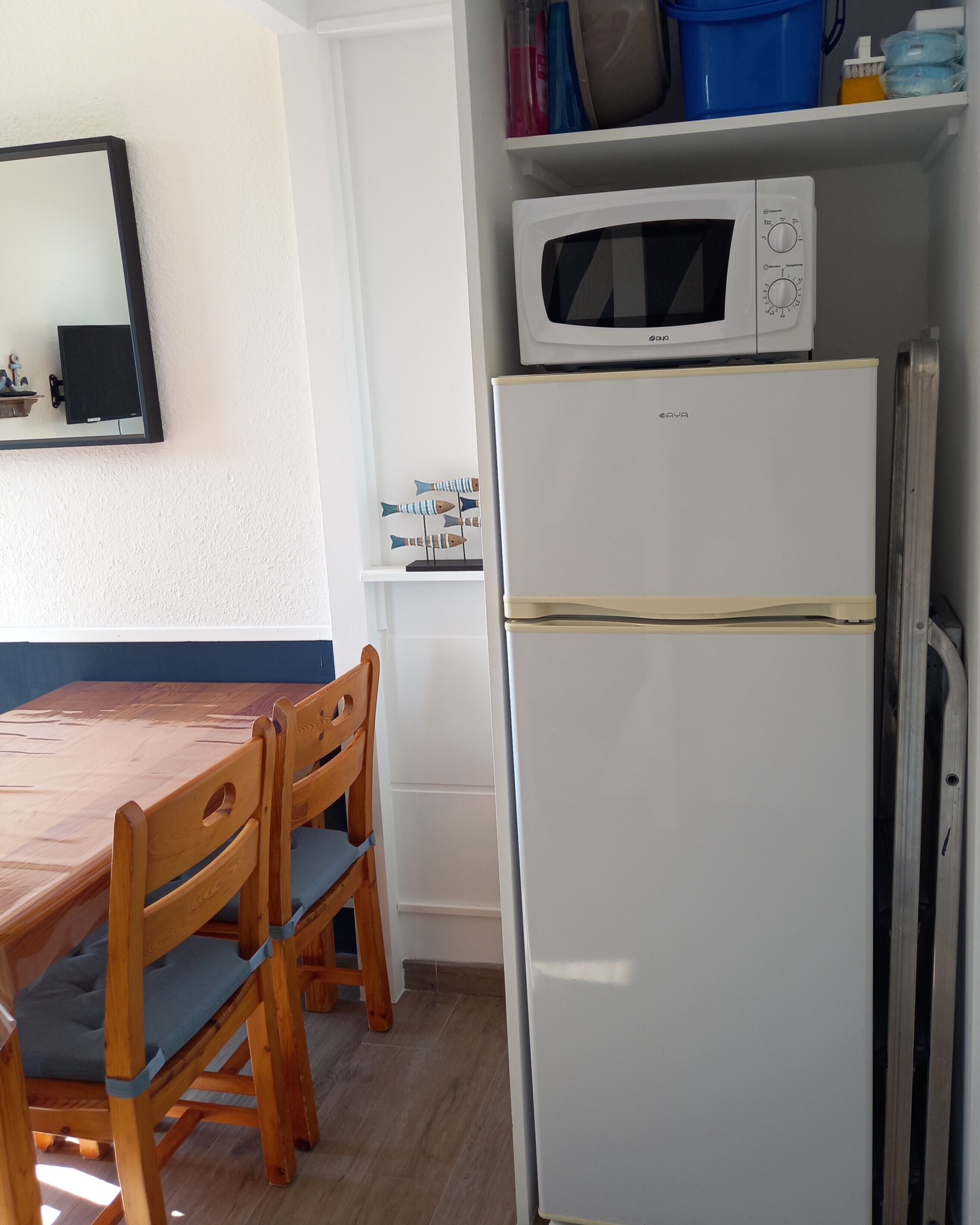 Una cocina compacta con un refrigerador blanco, un microondas y una mesa de comedor de madera con sillas.