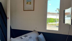 A room with a white and blue sofa, a framed picture on the wall, and a window with a view of greenery. - Atlantique 165 (La Faute-sur-Mer)