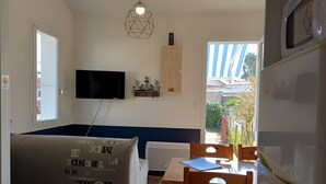 A compact living space with a sofa, dining table, chairs, a television, and a refrigerator. - Atlantique 165 (La Faute-sur-Mer)