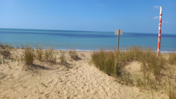 A sandy beach path leading to the ocean with a red and white striped pole and a blank signpost. - Atlantique 165 (La Faute-sur-Mer)