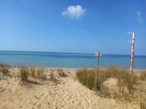 Un sentiero sabbioso che conduce verso l'oceano, con un palo a righe rosse e bianche e un cartello vuoto.