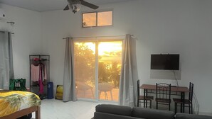 A room with a bed, a sofa, a TV, a ceiling fan, a window with curtains, and a view of the outdoors. - Perla Pacifico (Puerto Armuelles)