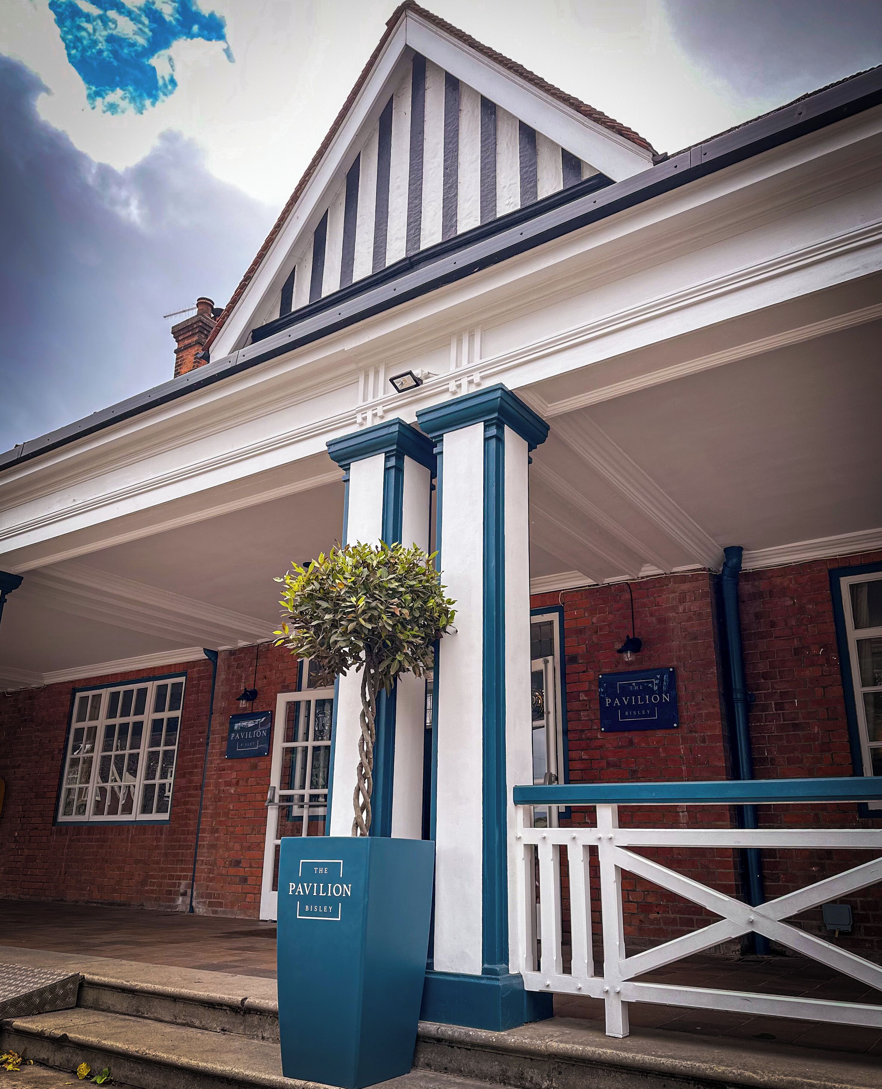 A building with a white facade, blue trim, and a sign reading "The Pavilion Bisley."
