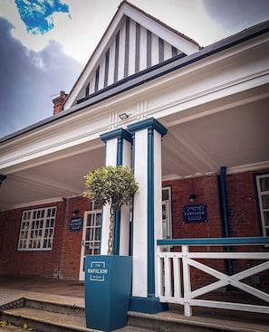 A building with a white facade, blue trim, and a sign reading "The Pavilion Bisley." - The Pavilion Bisley (Woking)