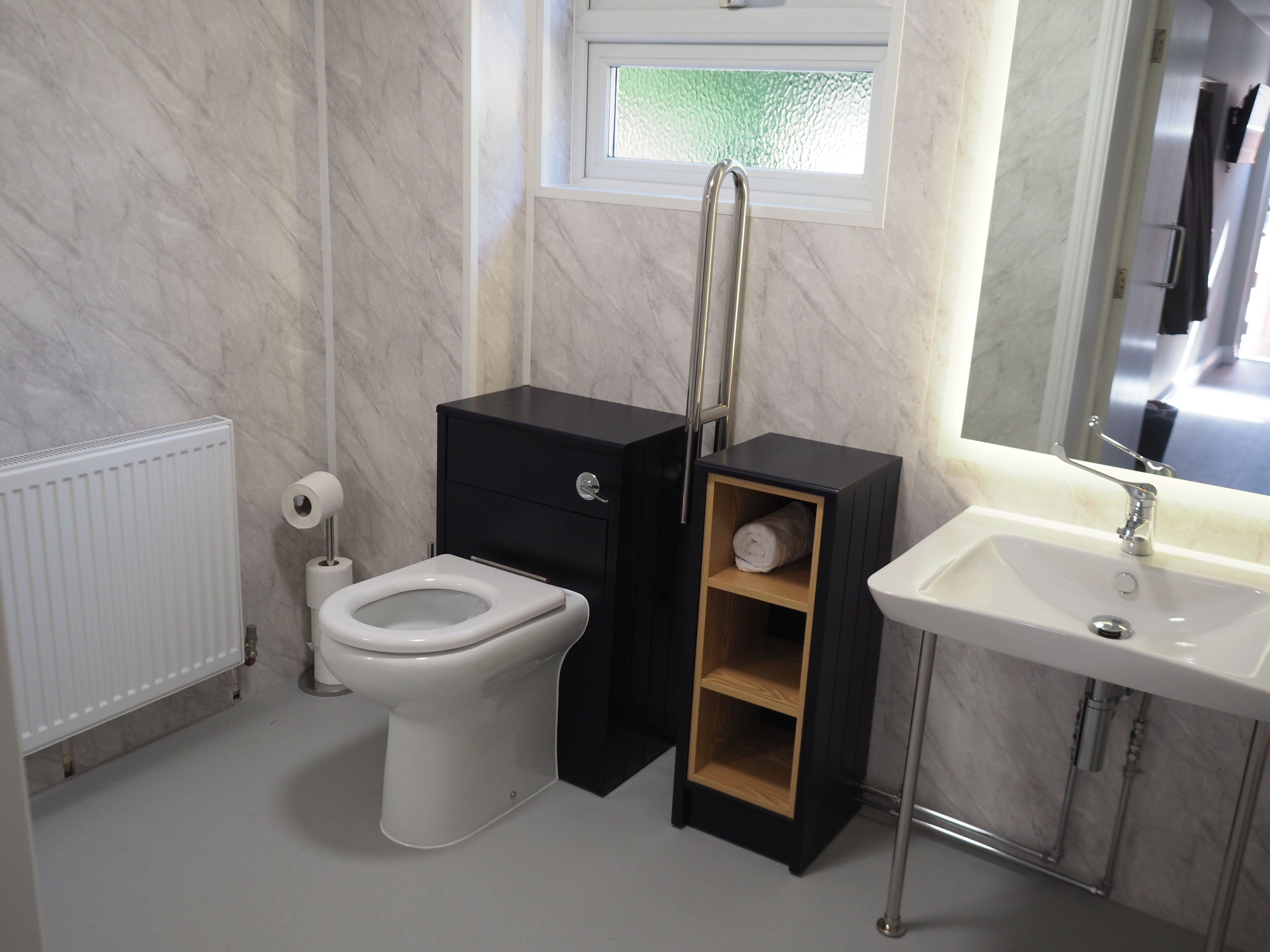 A modern bathroom with a toilet, a black cabinet with a wooden shelf, a white sink, and a mirror above the sink.