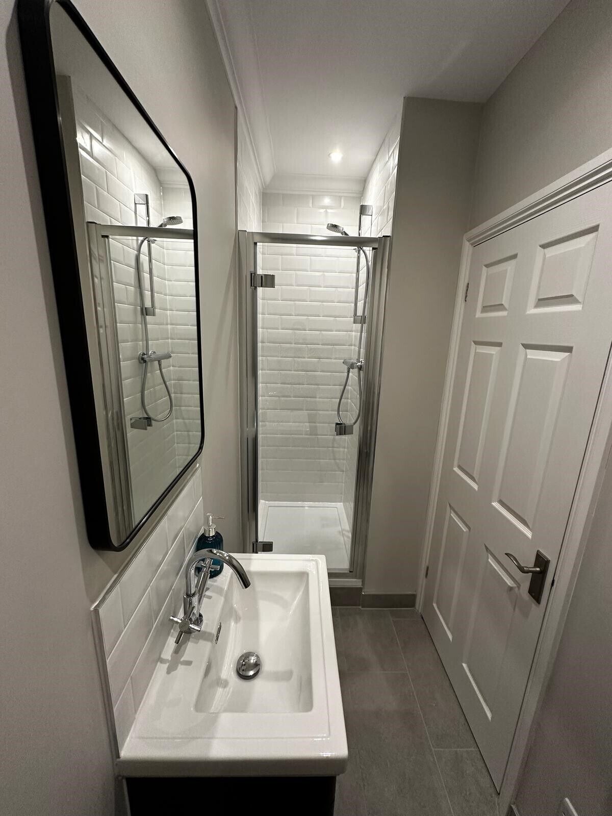 A modern bathroom with a white sink, mirror, and shower enclosure.