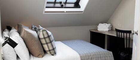 A bedroom with a skylight, a bed with multiple pillows, a bedside table with towels, and a chair.