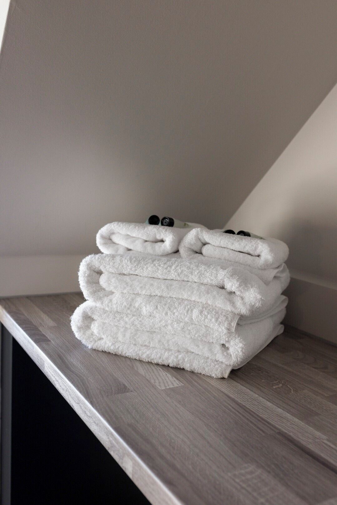 Une pile de serviettes blanches est posée sur une surface en bois dans une pièce dont le plafond est en pente.