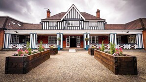 A traditional building with a symmetrical facade, a central entrance, and a gravel driveway. - The Pavilion Bisley (Woking)
