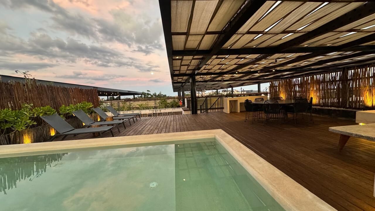 Un espace piscine avec des chaises longues, une terrasse en bois et un coin salon abrité.
